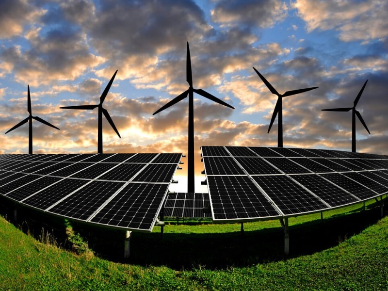 A landscape featuring solar panels and wind turbines under a dramatic sky.